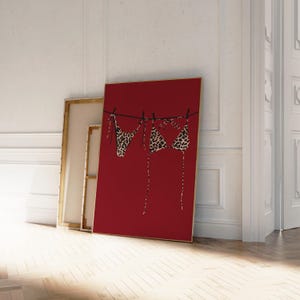 May include: A red canvas print with a leopard print bikini hanging on a clothesline. The bikini is hanging on a red background.