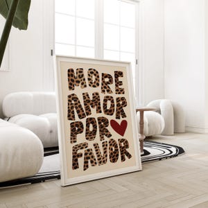 May include: A framed print with a beige background and the text "MORE AMOR POR FAVOR" in large, bold, black letters with a leopard print pattern. A red heart is in the center of the text.