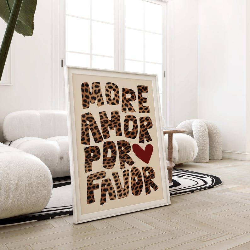 May include: A framed print with a beige background and the text "MORE AMOR POR FAVOR" in large, bold, black letters with a leopard print pattern. A red heart is in the center of the text.