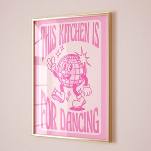 May include: Pink framed poster with a white disco ball character dancing and the text "This Kitchen is for Dancing".