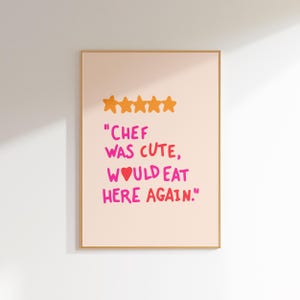 May include: A framed print with a peach background and gold frame. The print features five gold stars and text that reads "Chef was cute, would eat here again."