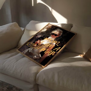 May include: A framed print of a woman wearing sunglasses and a white dress, holding a glass of wine. The text "MOM, I AM A RICH MAN" is written in yellow on the print.