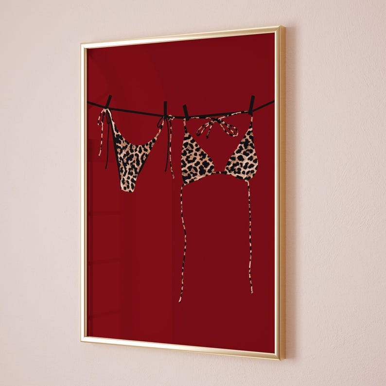 May include: A pair of leopard print bikini tops and bottoms hanging on a clothesline against a red background.