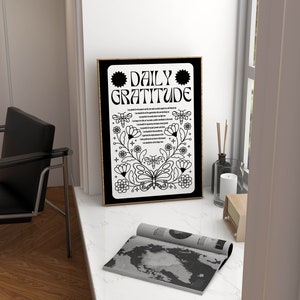 May include: A black and white framed print with the text "DAILY GRATITUDE" in a decorative font. The print features a butterfly and floral designs.