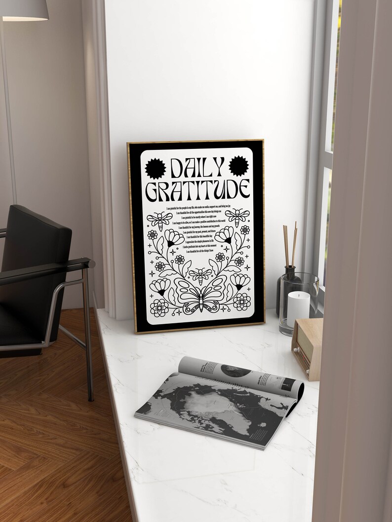 May include: A black and white framed print with the text "DAILY GRATITUDE" in a decorative font. The print features a butterfly and floral designs.