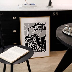 Puede incluir: Un p&oacute;ster en blanco y negro con un dise&ntilde;o floral y el texto "Grow Through What You Go Through". El p&oacute;ster est&aacute; enmarcado en un marco dorado y est&aacute; colgado en una pared negra.