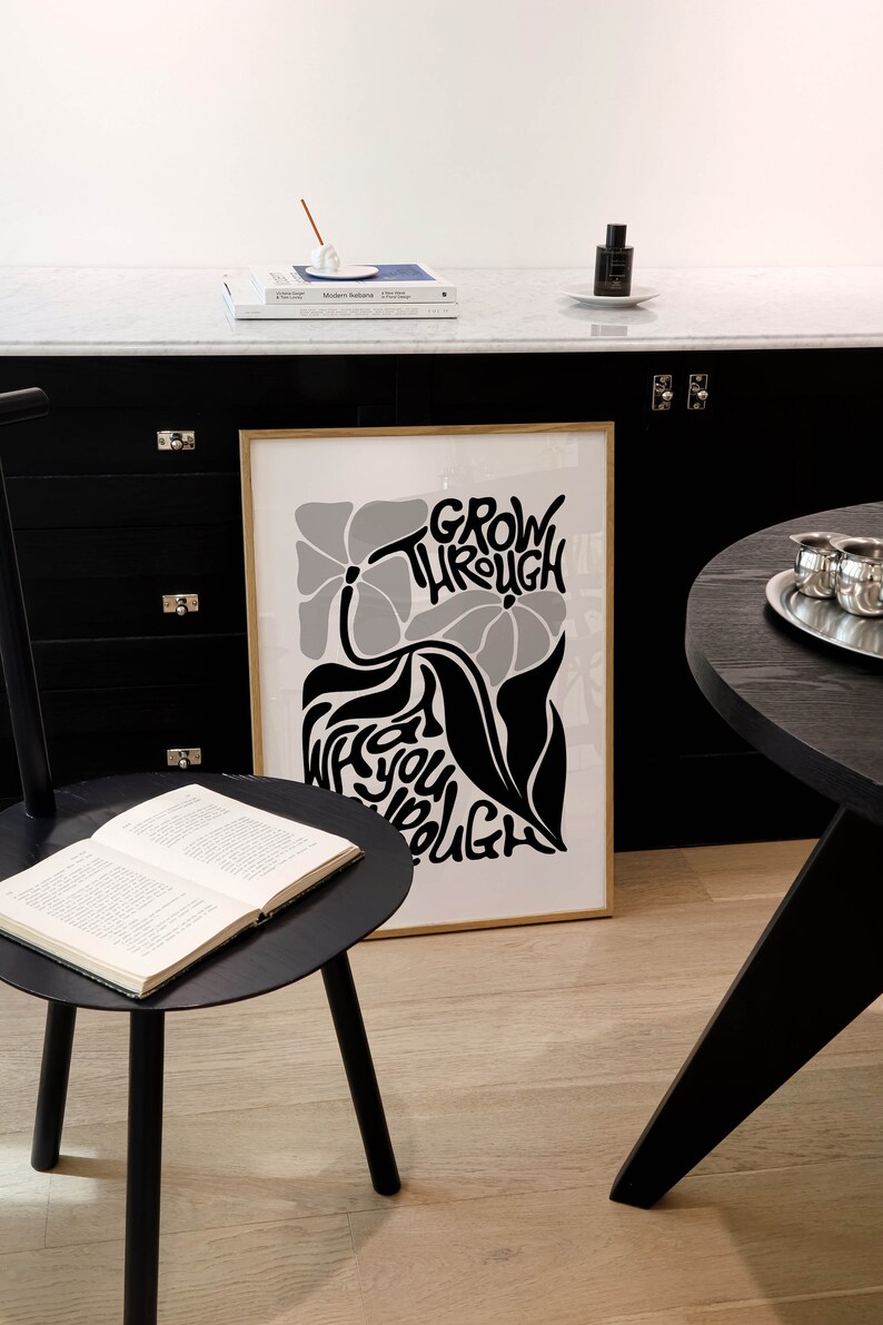 Puede incluir: Un p&oacute;ster en blanco y negro con un dise&ntilde;o floral y el texto "Grow Through What You Go Through". El p&oacute;ster est&aacute; enmarcado en un marco dorado y est&aacute; colgado en una pared negra.