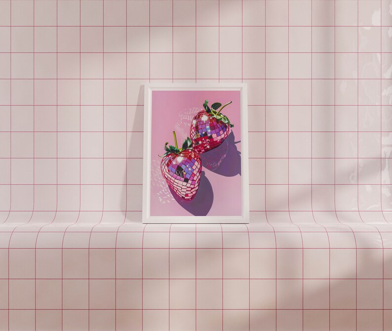 May include: Two pink disco ball strawberries in a white frame against a pink tiled background.