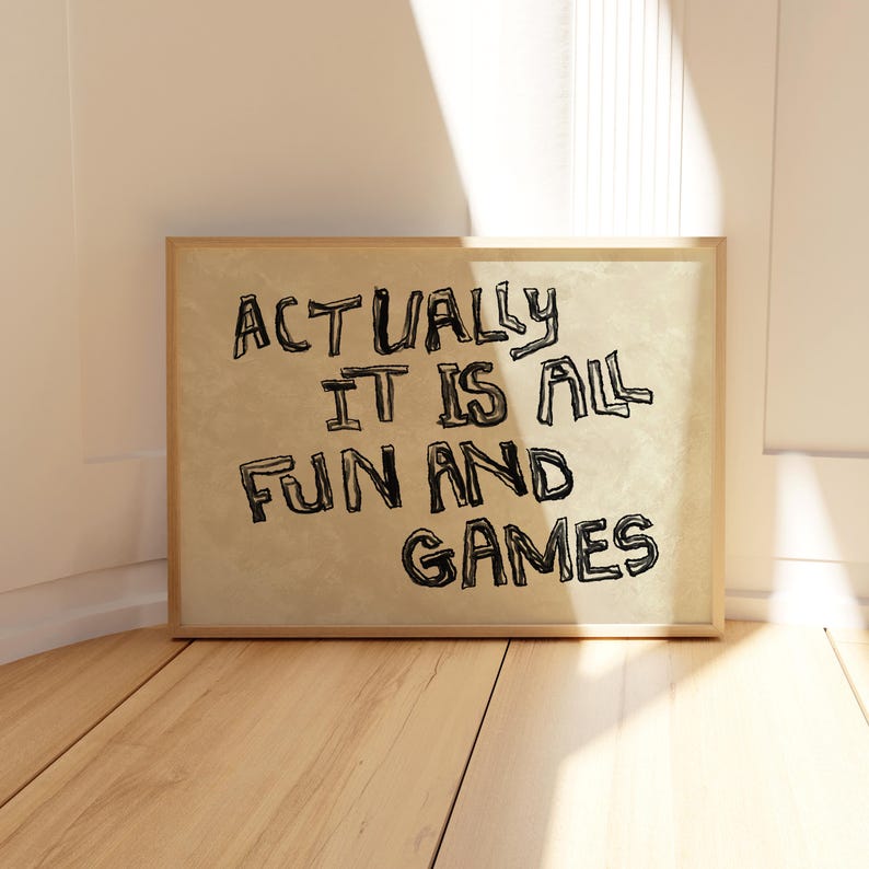 Pode incluir: Uma impress&atilde;o emoldurada com o texto "ACTUALLY IT IS ALL FUN AND GAMES" em letras pretas manuscritas. A impress&atilde;o tem um fundo bege e uma moldura de madeira castanho-claro. A impress&atilde;o &eacute; exibida em um piso de madeira.