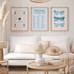 May include: Three framed prints on a white wall. The left print is a blue ace of hearts playing card. The middle print is a light blue background with the text "Ways to Say I Love You" in blue. The right print is a light blue background with three pairs of blue sunglasses.