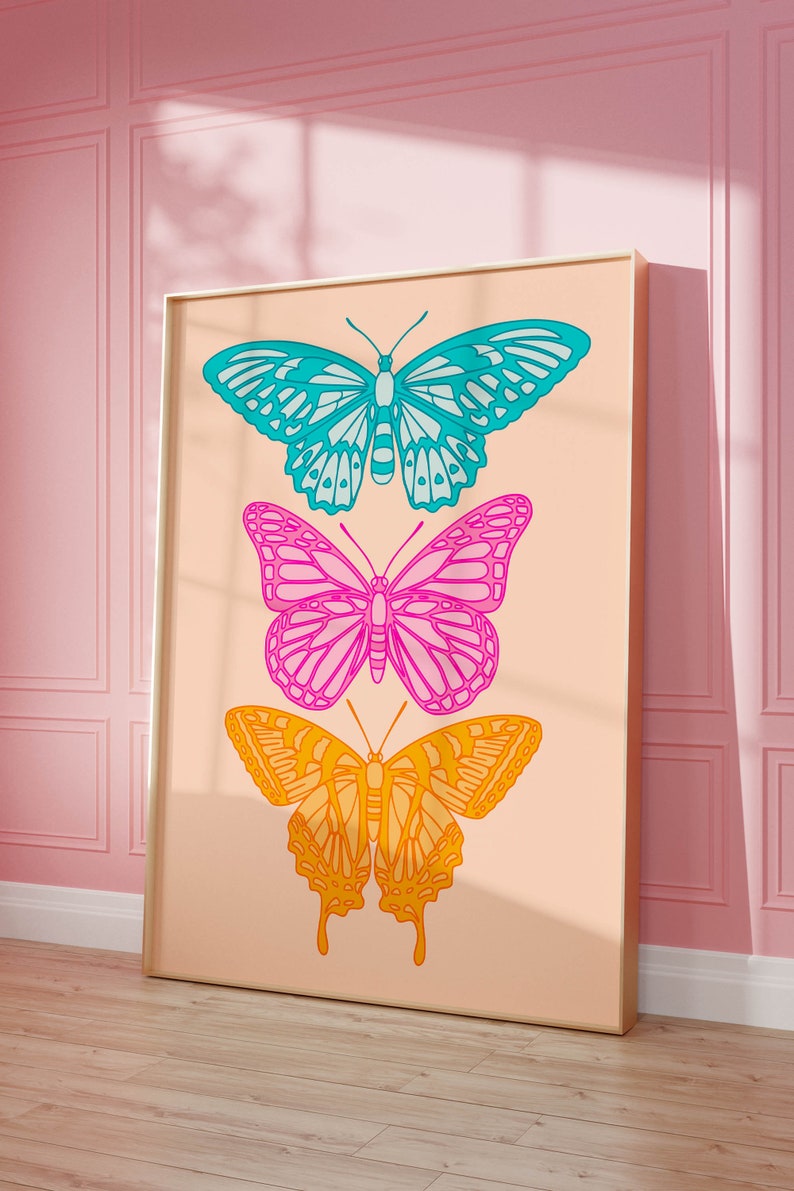 Pode incluir: Uma impress&atilde;o emoldurada com tr&ecirc;s borboletas coloridas em um fundo p&ecirc;ssego. As borboletas est&atilde;o sobrepostas, a borboleta superior &eacute; azul e verde, a borboleta do meio &eacute; rosa e roxa, e a borboleta inferior &eacute; laranja e amarela.