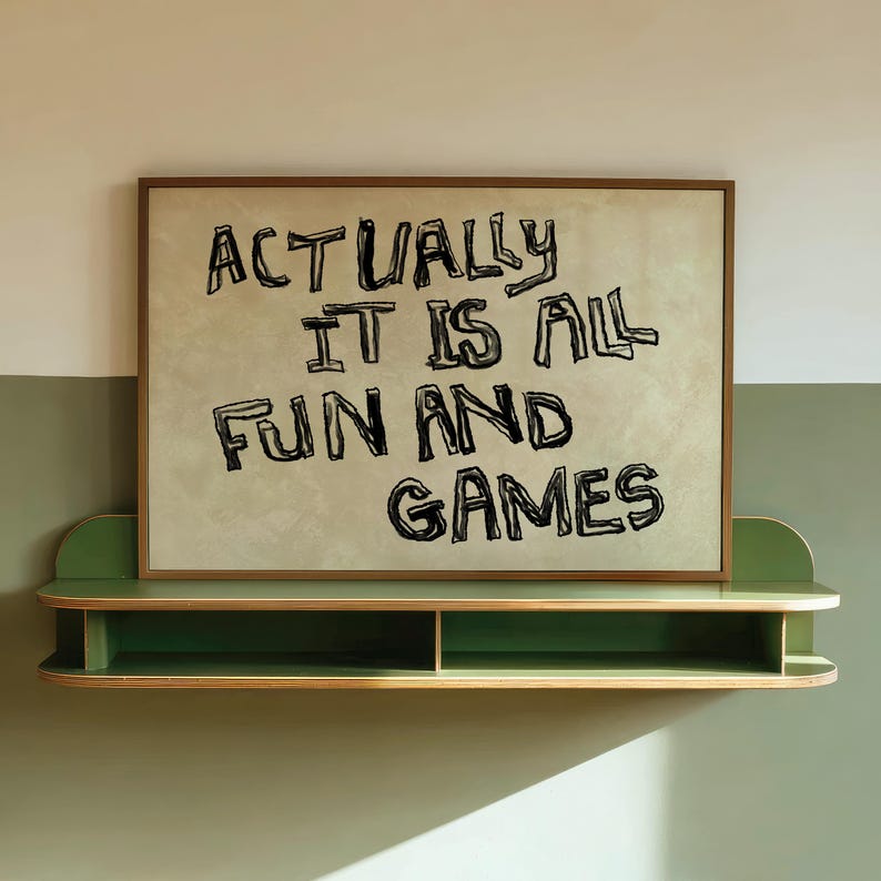 Pode incluir: Uma impress&atilde;o emoldurada com o texto "ACTUALLY IT IS ALL FUN AND GAMES" em preto, exibida acima de uma prateleira verde. A impress&atilde;o tem um fundo bege claro e uma moldura marrom. A prateleira &eacute; verde com borda de madeira natural.