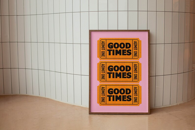 May include: A framed print featuring three orange tickets on a pink background. Each ticket reads "Good Times" and "Admit One".