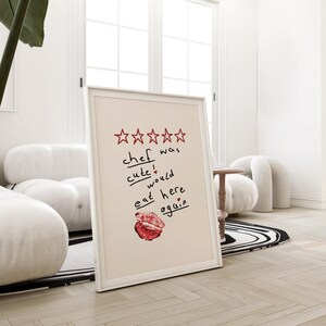 Op de afbeelding: Een ingelijst afdruk met een vijfsterrenbeoordeling en de tekst "kok was schattig! zou hier weer eten" met een rood hart en een rode lippenstiftkus.
