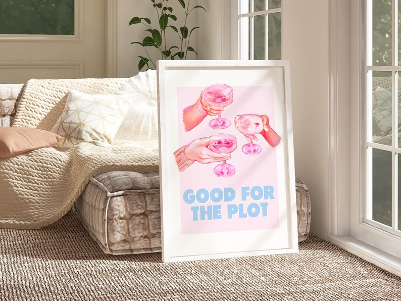 May include: A white framed print with a pink background and a watercolor illustration of three hands holding pink cocktails. The text "GOOD FOR THE PLOT" is written in blue letters below the illustration.