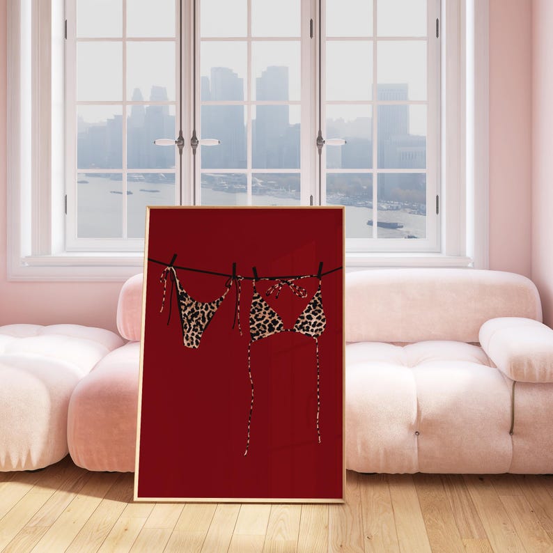 May include: A framed print of a leopard print bikini hanging on a clothesline against a red background.