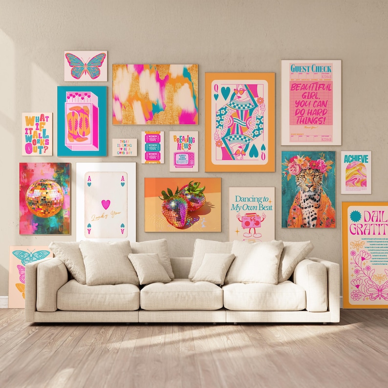 May include: A collage of colorful wall art prints featuring various designs, including a disco ball, a butterfly, a playing card, a strawberry, a leopard, and text-based prints. The prints are arranged on a wall above a white couch.
