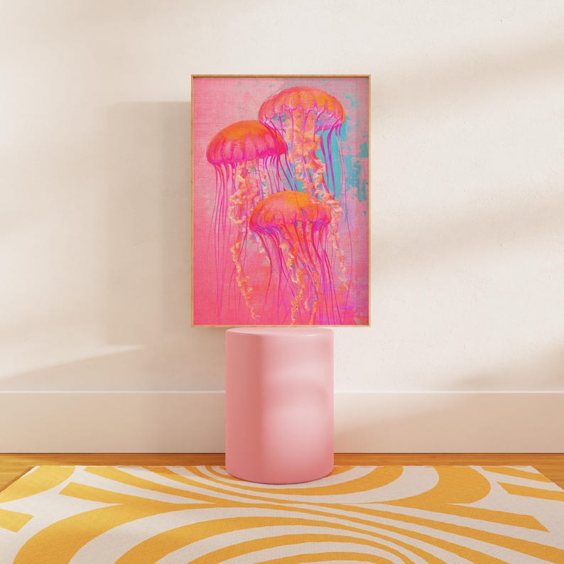 May include: A framed print of three pink jellyfish with long tentacles against a pink and blue background. The print is displayed on a pink pedestal.