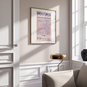 K&ouml;nnte beinhalten: Ein gerahmter Druck eines rosa Gastchecks mit dem Text "You're like really pretty" in blau. Der Druck h&auml;ngt an einer wei&szlig;en Wand in einem Raum mit einem Sofa und einer Lampe.