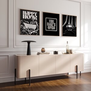 Pode incluir: Tr&ecirc;s impress&otilde;es emolduradas em preto e branco penduradas em uma parede branca acima de um arm&aacute;rio bege claro. As impress&otilde;es apresentam o texto "Happy Hour", "The Bar's Open" e uma bola de discoteca.