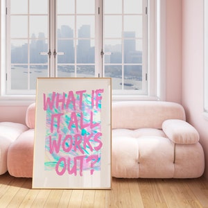 Puede incluir: Un cuadro enmarcado con el texto "WHAT IF IT ALL WORKS OUT?" en rosa sobre un fondo abstracto colorido. La obra de arte se exhibe en una habitaci&oacute;n con un sof&aacute; y paredes rosas, y una ventana con vistas a un paisaje urbano.