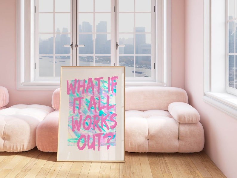 Puede incluir: Un cuadro enmarcado con el texto "WHAT IF IT ALL WORKS OUT?" en rosa sobre un fondo abstracto colorido. La obra de arte se exhibe en una habitaci&oacute;n con un sof&aacute; y paredes rosas, y una ventana con vistas a un paisaje urbano.