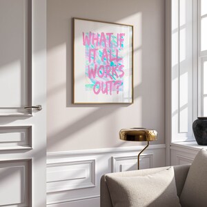 Puede incluir: Un cuadro enmarcado con el texto "WHAT IF IT ALL WORKS OUT?" en rosa y azul sobre un fondo blanco. La obra de arte est&aacute; en un marco dorado y cuelga de una pared clara. Una l&aacute;mpara dorada y un sof&aacute; est&aacute;n en primer plano.