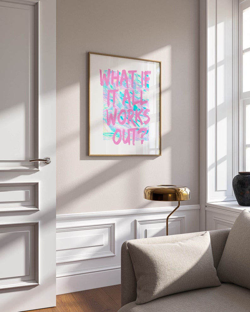 Puede incluir: Un cuadro enmarcado con el texto "WHAT IF IT ALL WORKS OUT?" en rosa y azul sobre un fondo blanco. La obra de arte est&aacute; en un marco dorado y cuelga de una pared clara. Una l&aacute;mpara dorada y un sof&aacute; est&aacute;n en primer plano.