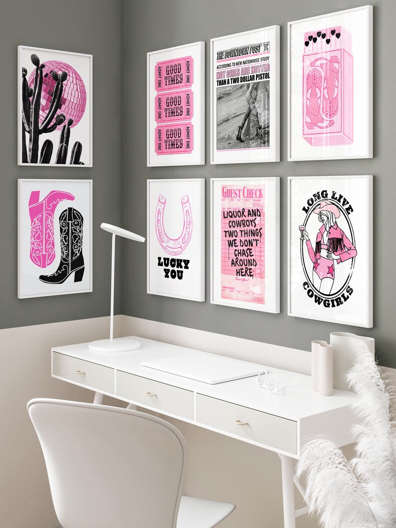 May include: A collection of eight pink and black framed prints with various designs, including a disco ball, a horseshoe, a cowboy boot, a guest check, and a cowgirl. The prints are hanging on a gray wall above a white desk with a white chair.