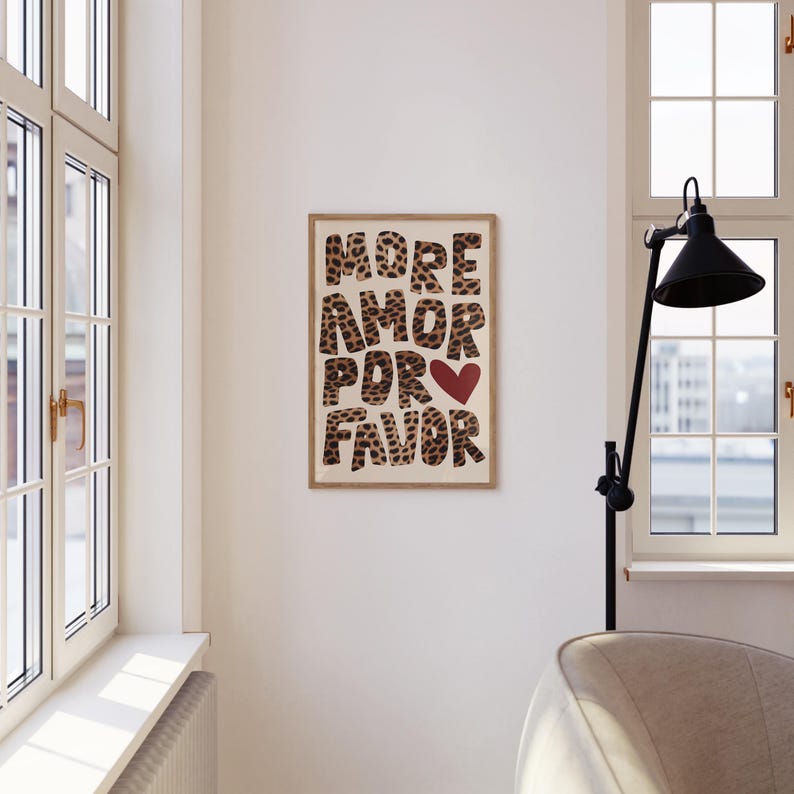 May include: A framed print with the text "MORE AMOR POR FAVOR" in a leopard print font with a red heart in the middle of the text. The print is hanging on a white wall.