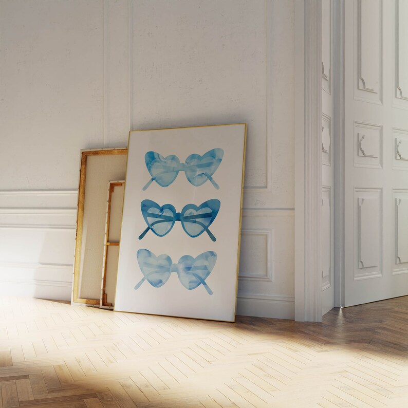 May include: A framed print of three watercolor illustrations of blue heart-shaped sunglasses. The sunglasses are arranged vertically in a row.