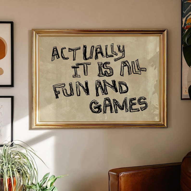 Pode incluir: Uma impress&atilde;o emoldurada com o texto "ACTUALLY IT IS ALL FUN AND GAMES" em letras pretas, estilo manuscrito. A moldura &eacute; dourada e o fundo da impress&atilde;o &eacute; bege claro. A impress&atilde;o est&aacute; pendurada em uma parede de cor neutra.