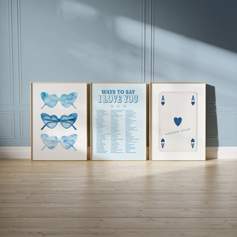 May include: Three framed prints with a blue and white color scheme. The left print features three pairs of blue heart-shaped sunglasses. The middle print has a list of ways to say "I love you" in blue text on a light blue background. The right print is a white playing card with a blue heart and the text "amore mio".