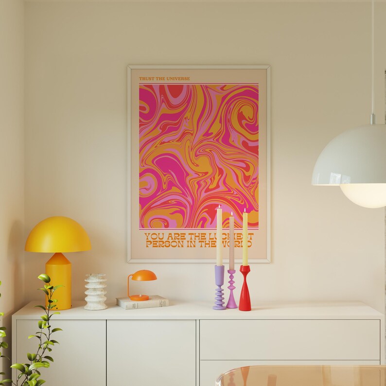 Peut inclure: Une affiche encadr&eacute;e avec un motif abstrait en spirale rose, orange et jaune. Le texte "Trust the Universe" et "You are the Lightest Person in the World" est imprim&eacute; sur l'affiche.