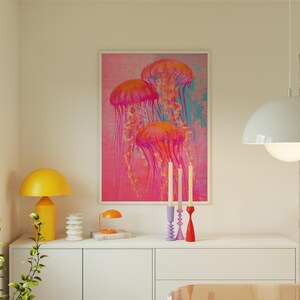 May include: A framed print of three pink and orange jellyfish against a pink and blue background. The print is hanging on a white wall above a white dresser with three candlesticks and candles.