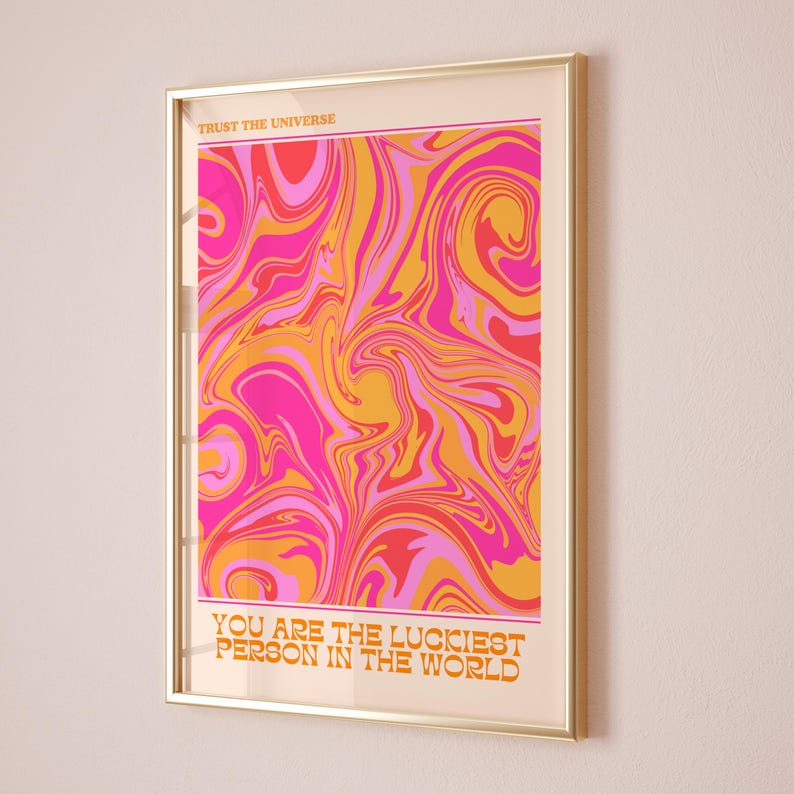 Peut inclure: Une impression encadr&eacute;e avec un motif abstrait en spirale rose, orange et jaune. Le texte "Trust the Universe" est en haut et "You are the luckiest person in the world" est en bas.