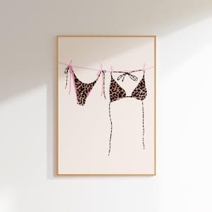 May include: A leopard print bikini hanging on a clothesline with pink string. The bikini is made of a soft, stretchy fabric and has a classic triangle top and a cheeky bottom.