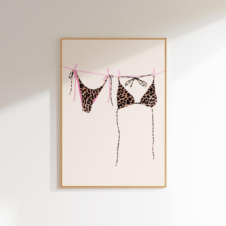 May include: A leopard print bikini hanging on a clothesline with pink string. The bikini is made of a soft, stretchy fabric and has a classic triangle top and a cheeky bottom.