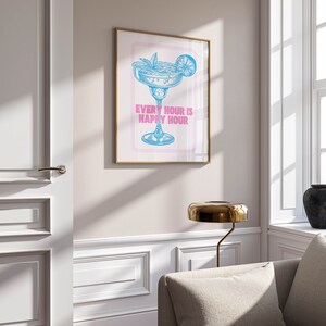 Puede incluir: Una impresi&oacute;n enmarcada con una ilustraci&oacute;n azul de una copa de margarita con una rodaja de lima y el texto "Every hour is happy hour" en rosa.