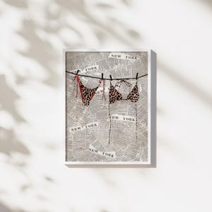 May include: A framed print of a leopard print bikini hanging on a clothesline made of twine. The background is a newspaper print with the words "NEW YORK" repeated throughout.