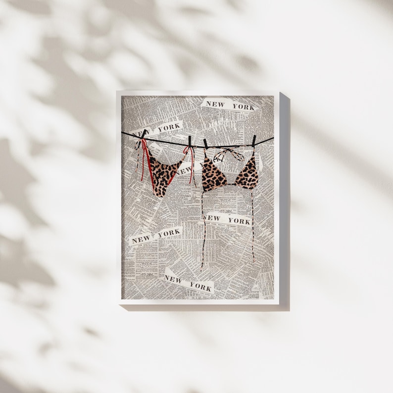 May include: A framed print of a leopard print bikini hanging on a clothesline made of twine. The background is a newspaper print with the words "NEW YORK" repeated throughout.