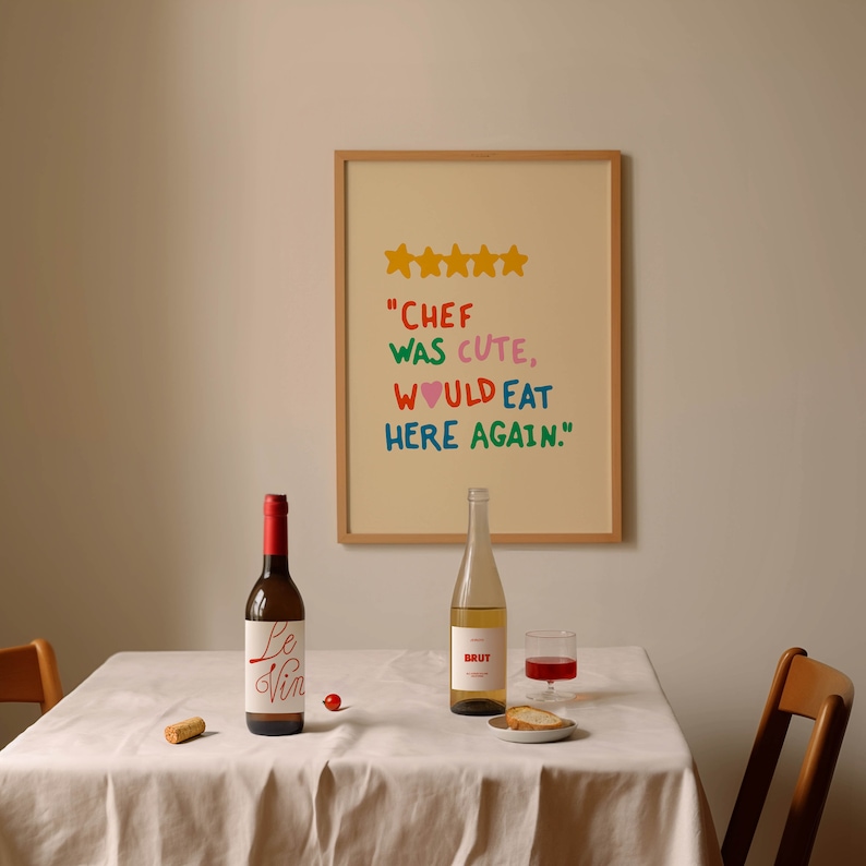 May include: A white tablecloth with two bottles of wine, one red and one white, and a glass of red wine. There is a plate with bread and a cork on the table. A framed picture with a five-star rating and the text "Chef was cute, would eat here again." is hanging on the wall behind the table.