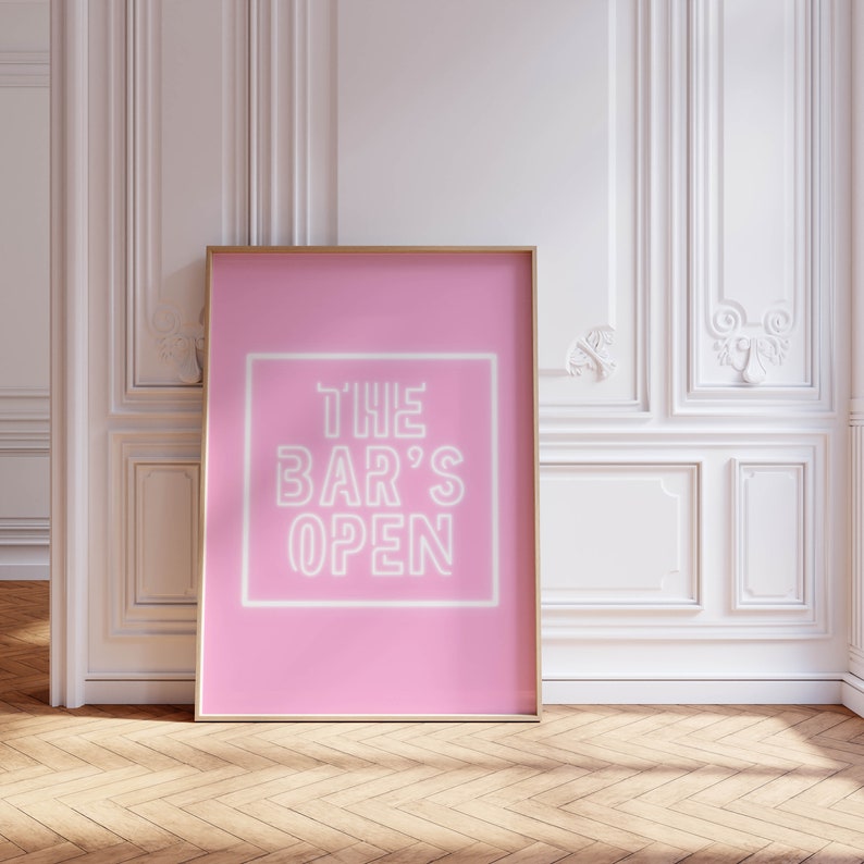 Puede incluir: Un p&oacute;ster rosa con un letrero de ne&oacute;n blanco que dice "THE BAR'S OPEN" en un marco blanco.