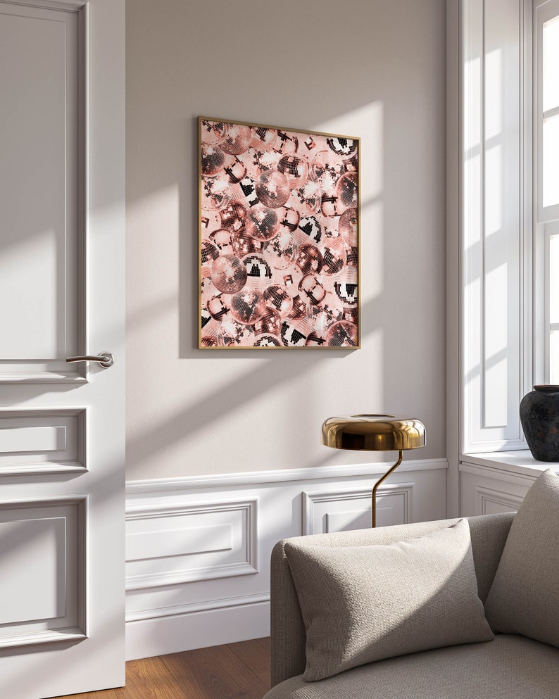 May include: A framed print of a pink and black disco ball pattern. The print is hanging on a white wall in a room with a white door and a couch.
