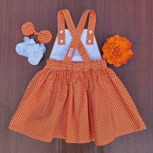 May include: Orange and white gingham dress with white straps and buttons. The dress has a white lining and a gathered skirt.