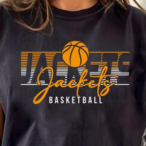 May include: Black t-shirt with the text "Jacket Basketball" in orange and white. The design includes a basketball graphic. The shirt is short-sleeved.