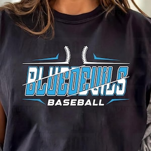 May include: Black t-shirt featuring the text "Blue Devils Baseball" in white and light blue, with a baseball graphic. The shirt has a crew neck and rolled-up sleeves.