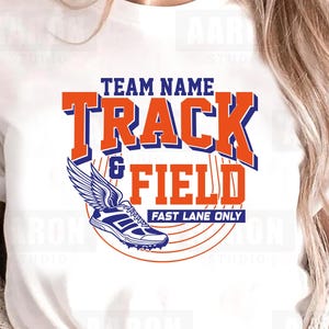 Puede incluir: Camiseta blanca con un diseño de atletismo. El diseño presenta las palabras "TRACK & FIELD" en naranja y azul, una zapatilla alada y el texto "FAST LANE ONLY".