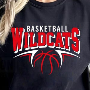 May include: Black t-shirt featuring the text "BASKETBALL WILDCATS" in red and white, with a basketball design. The shirt has a crew neck and short sleeves.