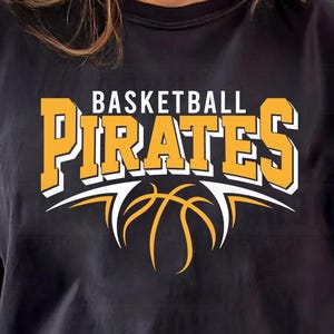 May include: Black t-shirt with the words "BASKETBALL PIRATES" in yellow and white lettering, with a basketball graphic. The shirt is worn by a person.